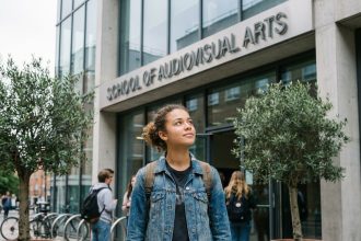 Jeune femme devant l'entrée d'une école d'audiovisuel après le bac, regardant le bâtiment avec confiance