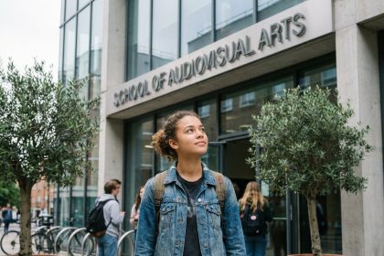 Jeune femme devant l'entrée d'une école d'audiovisuel après le bac, regardant le bâtiment avec confiance